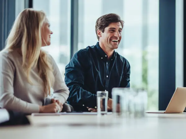 Mies ja nainen istuvat pöydän ääressä ja hymyilevät