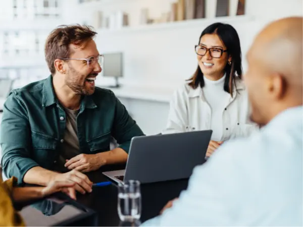 Kolme hymyilevää ihmistä istuu mustan pöydän ääressä