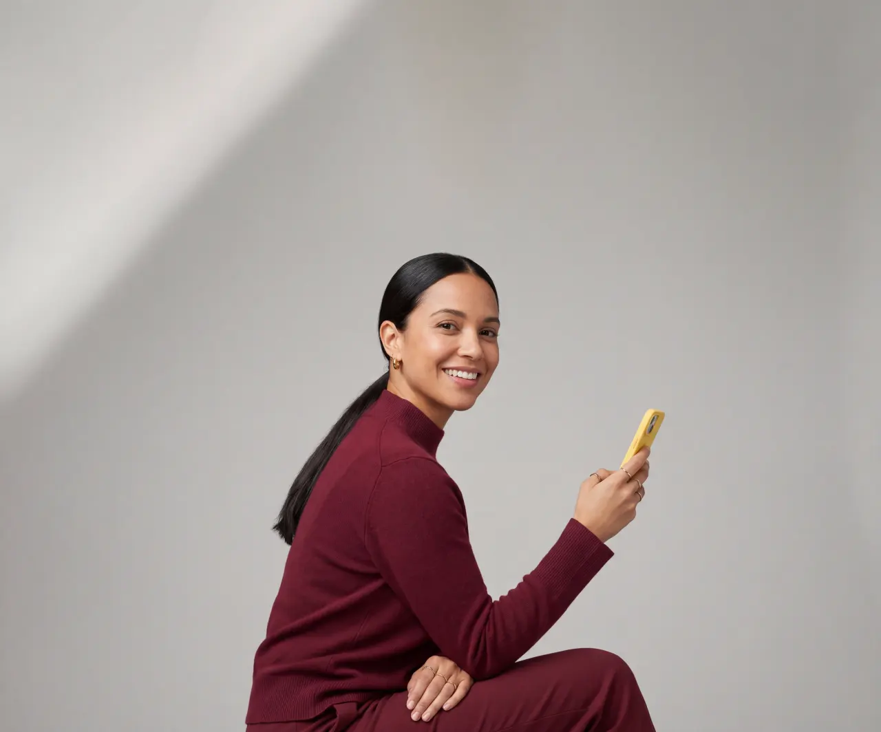 SDW_2026_Signature_smiling-woman-holding-yellow-phone_burgundy